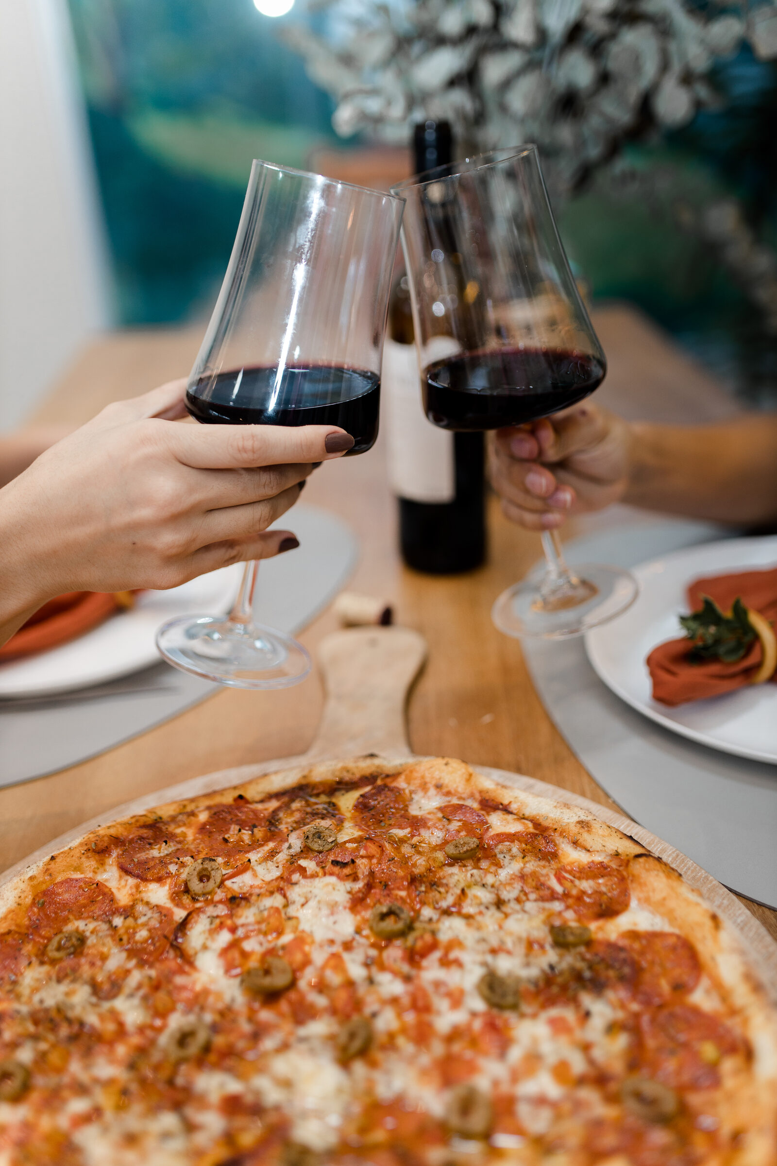 Duas pessoas brindando à mesa com uma pizza da Cia Casero